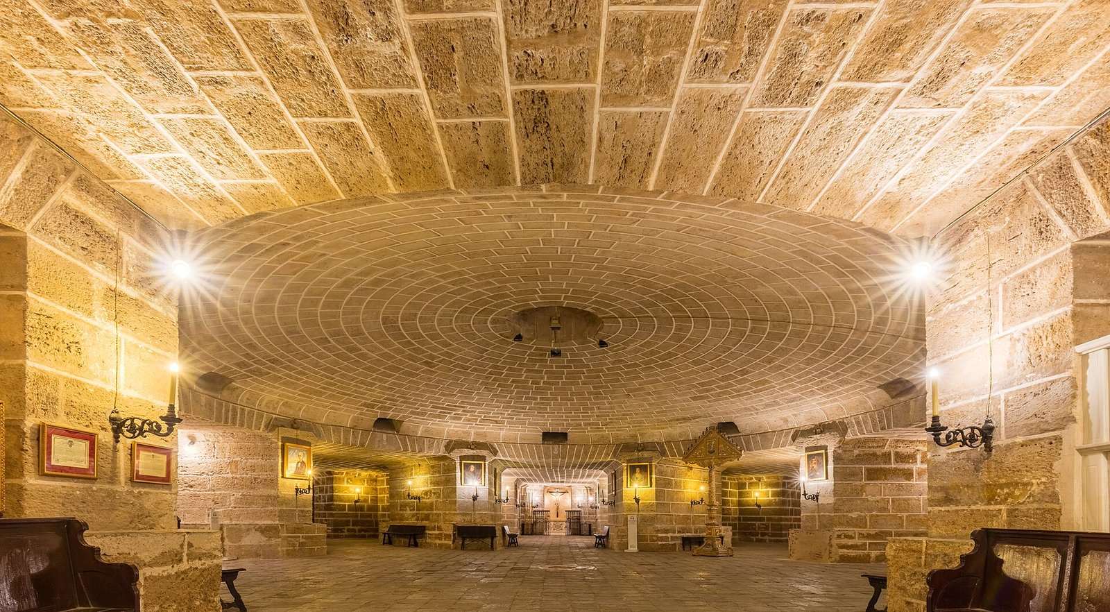 Cripta de piedra con bóveda circular de ladrillo y candelabros, en la Catedral de Cádiz.