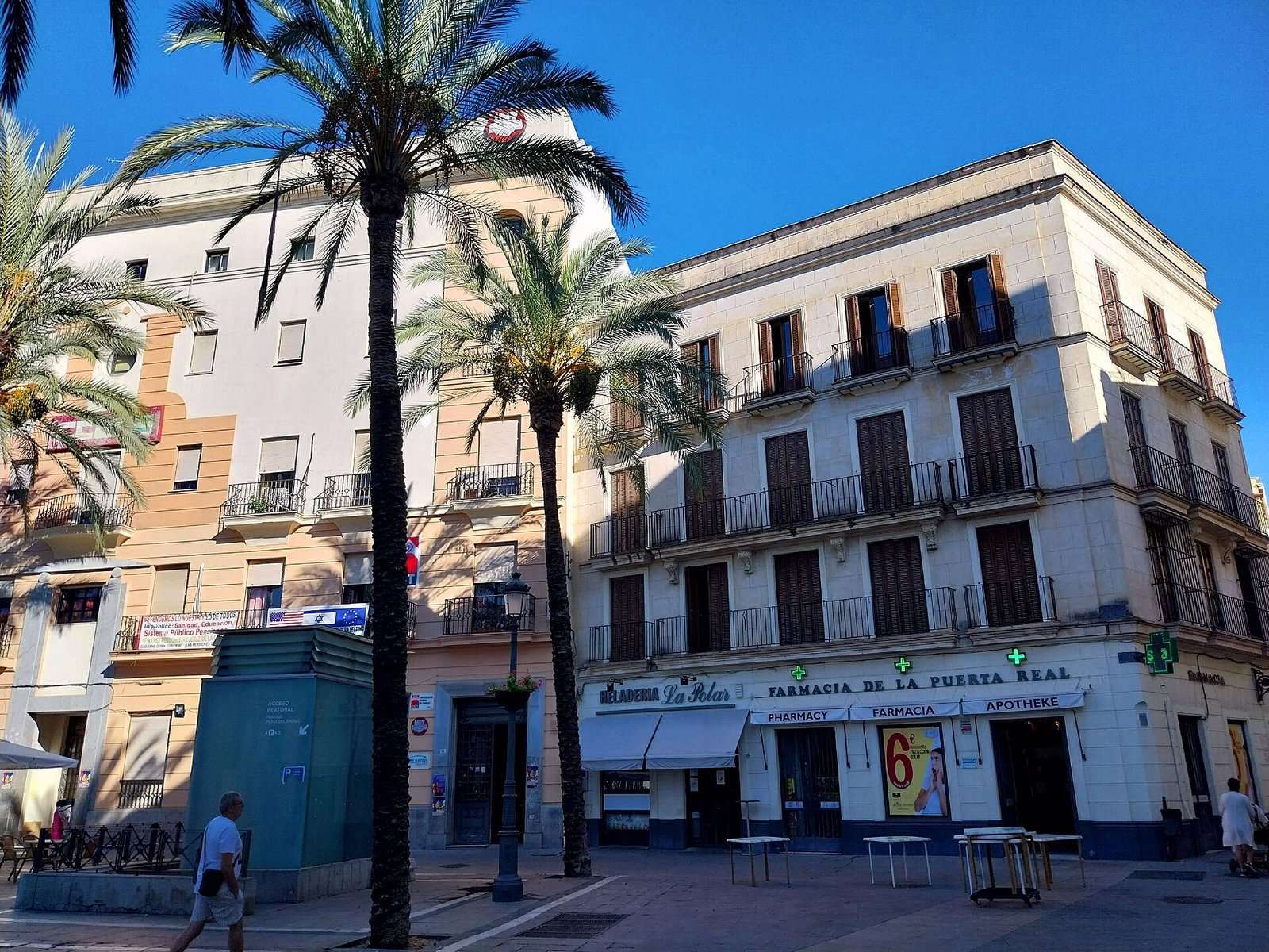 Edificios con balcones y palmeras en la plaza del Arenal de Jerez de la Frontera, con una farmacia y una heladería